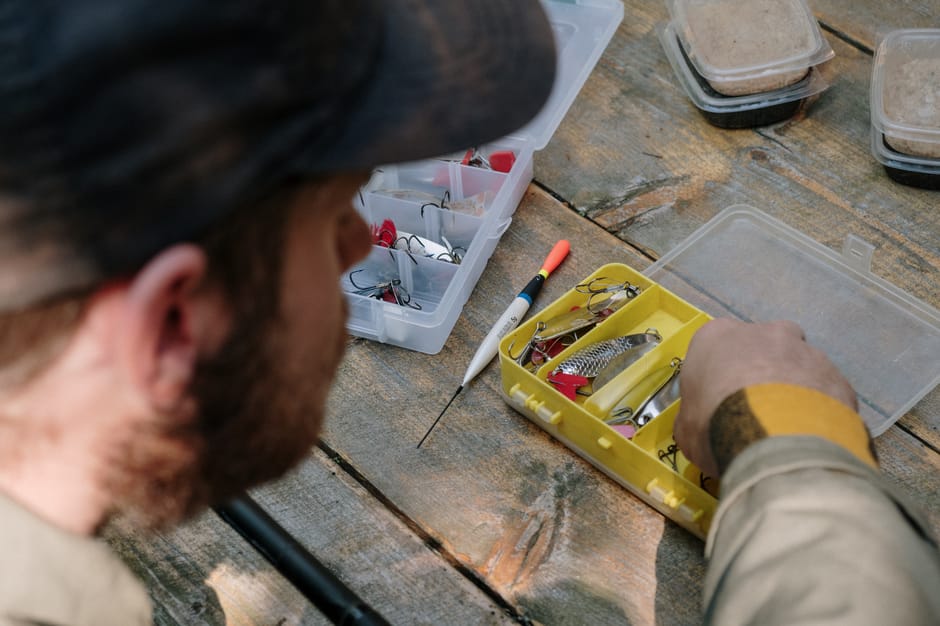 A person organizing fishing lures and tools on a rustic wooden surface outdoors.