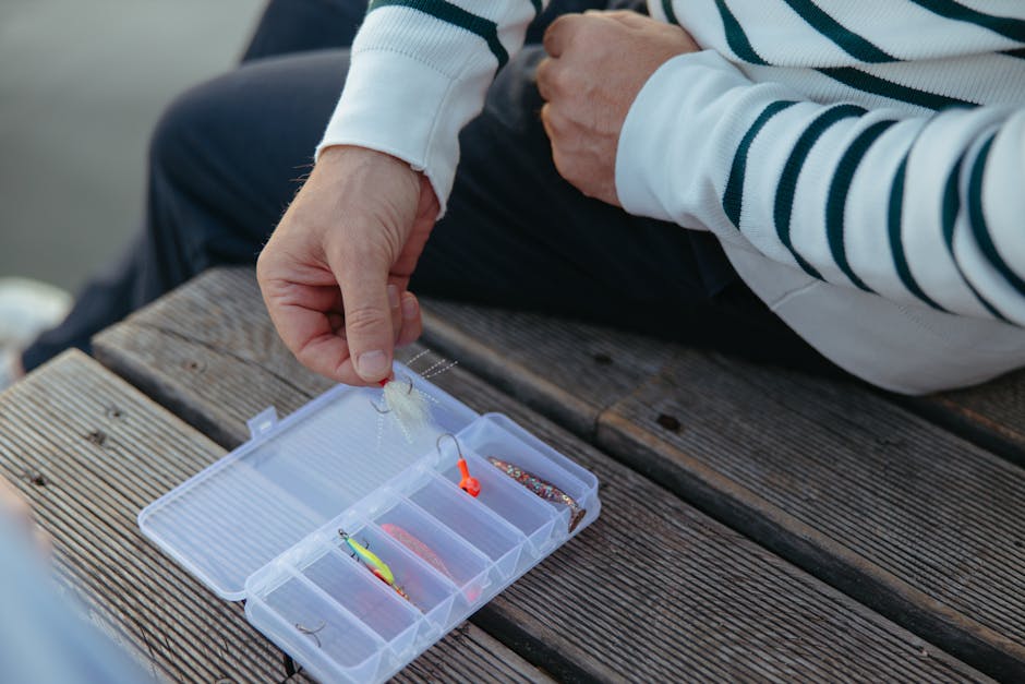 A person selects a fishing lure from a tackle box on a wooden dock, ready for fishing.