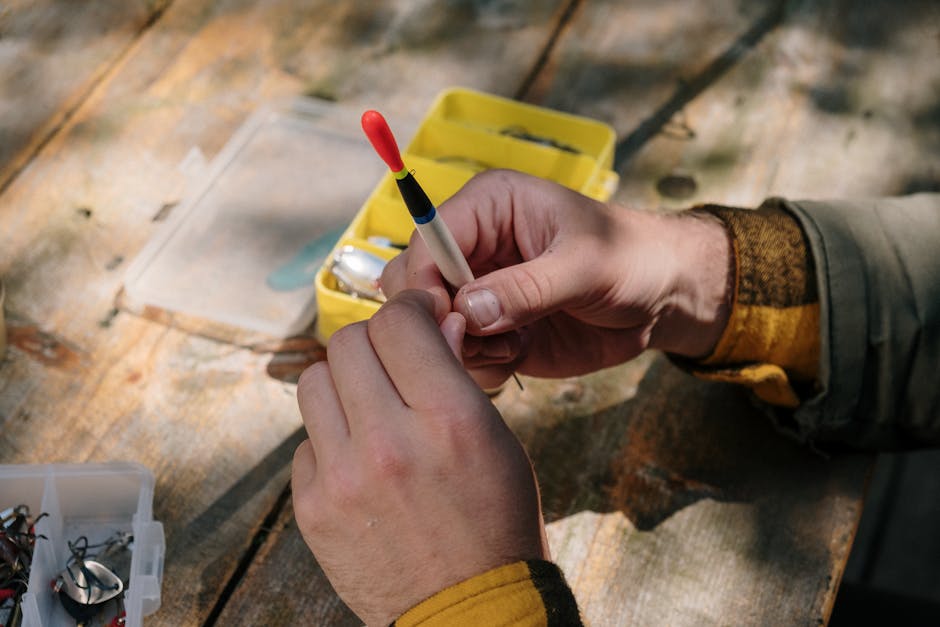 Hands preparing fishing tackle with lures and hooks on a wooden surface outdoors.